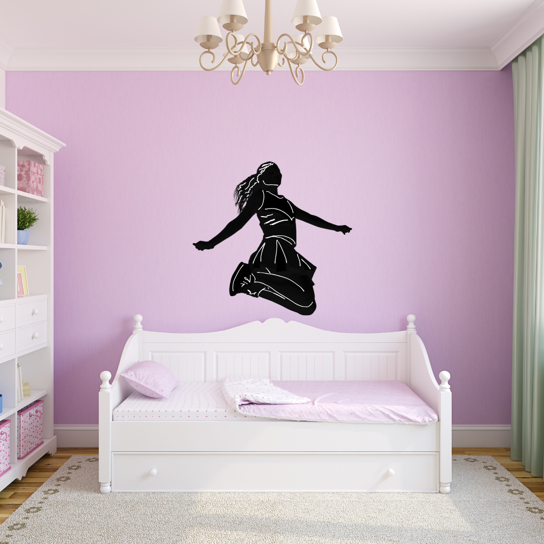 A black vinyl wall decal of a leaping girl cheerleader displayed on a lavender wall above a white wooden daybed.