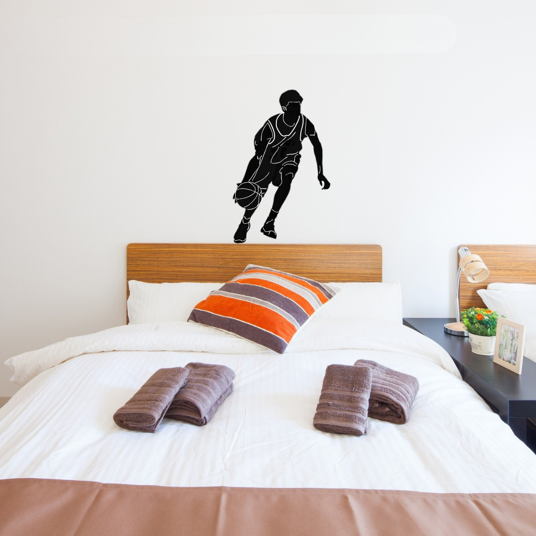 A custom black vinyl wall decal of a basketball player in motion applied to a white bedroom wall above a bed with white linens and a striped accent pillow.